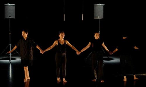 Four dancers with their eyes closed on a darkened stage
