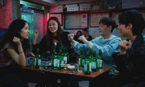 Four young Koreans have a good time around a table filled with empty soju bottles
