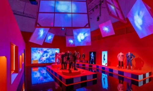 A room in the V+A's Hallyu exhibition: colourful red lighting with the outfits worn by various K-pop bands