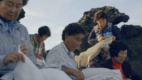 Several old women sit on the rocks holding a long swirl of fabric