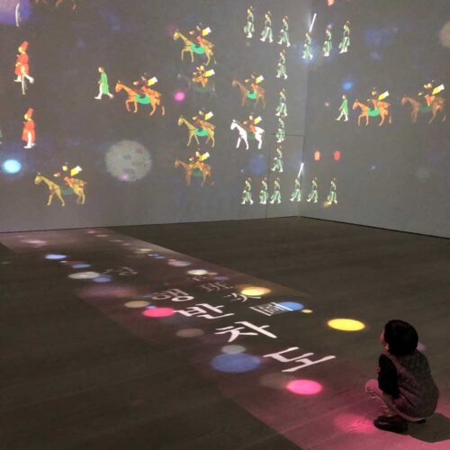 A boy squats while admiring a video projection