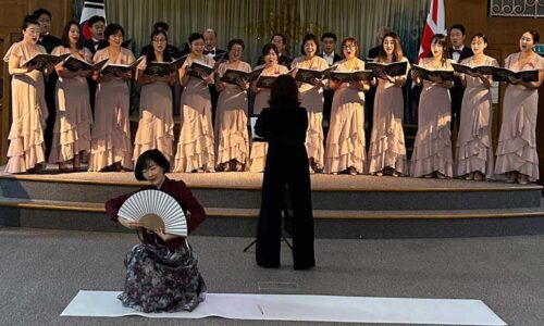 A Korean dancer performs a fan dance while a choir sings