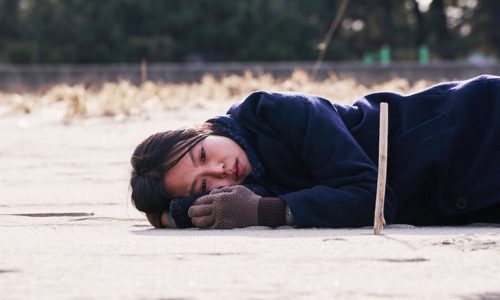 A young woman in an overcoat lying on white sand